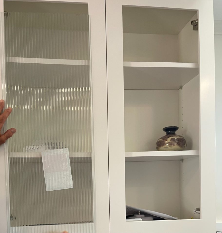 Revamp Your Kitchen Cabinets With Custom Glass Panels White cabinet with glass doors, displaying empty shelves and a decorative jar inside.