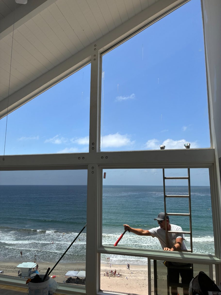 Geometrically-Shaped Picture Window Insulated Glass Replacement A worker cleaning a large window with a beach view in the background.