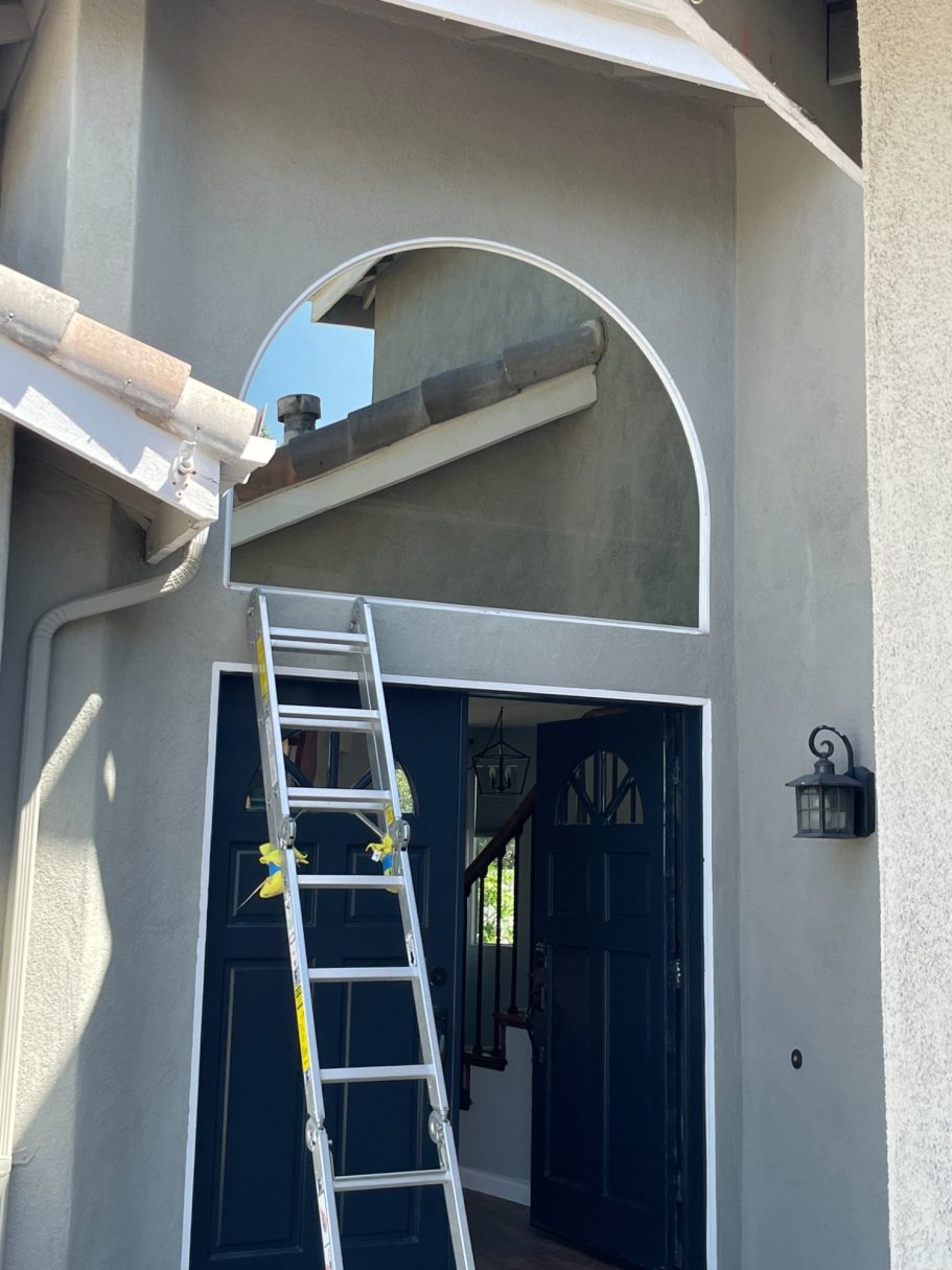 Template-Cut Glass for Window Opening Ladder positioned outside a house with an arched entryway and blue front doors.