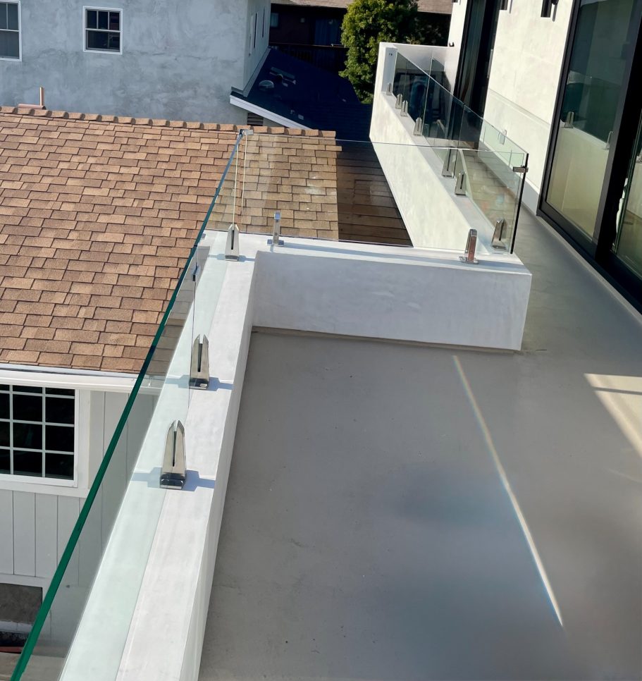 Glass Railing for Masonry Wall A modern balcony with glass railing overlooking a rooftop and nearby buildings.