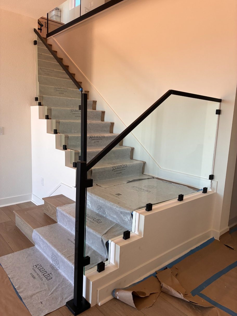 Stairwell Glass w/ Top Rail Modern staircase with glass railing and carpeted steps in a newly constructed home.